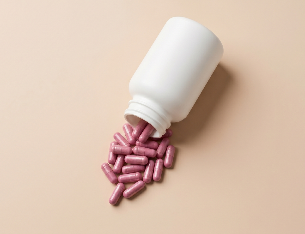 Wit potje supplementen met roze capsules op een beige achtergrond