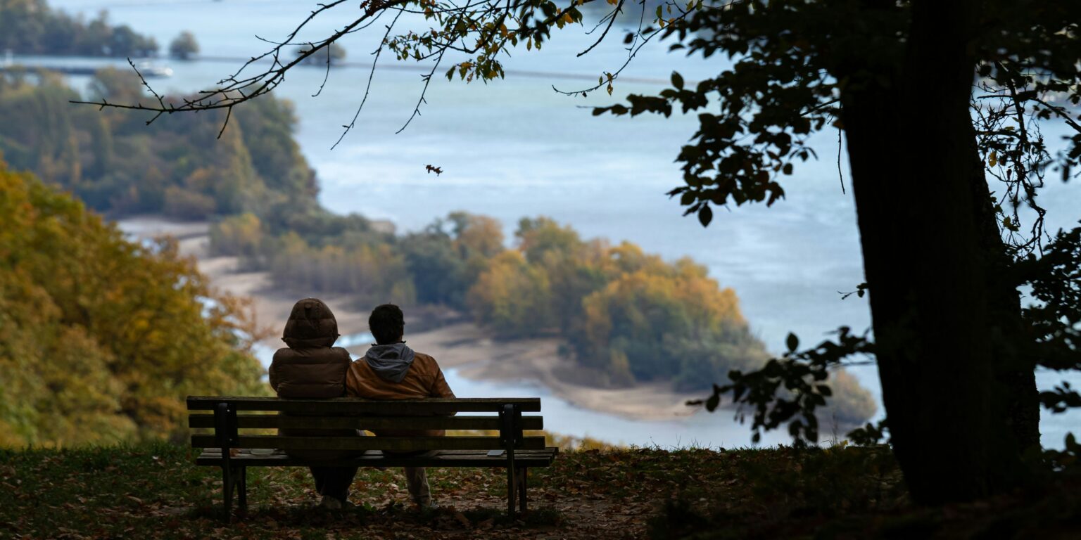 Twee mensen zittend op een bank met uitzicht op rivier in herfstkleuren