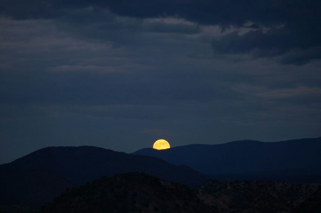 Volle gele maan rijst op boven donkere bergsilhouetten